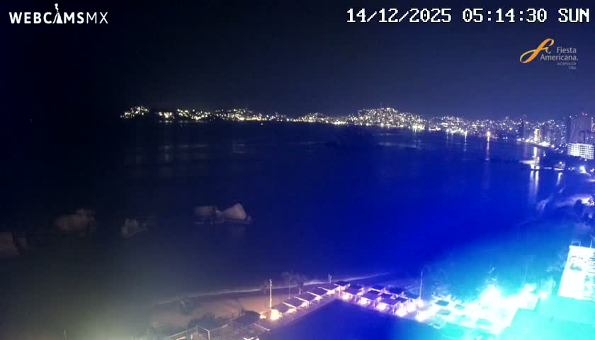 A nighttime aerial view overlooks a wide bay with a brightly illuminated city skyline stretching along the distant shore, while a resort's glowing swimming pool and covered cabanas line the immediate foreground under clear, dark skies.