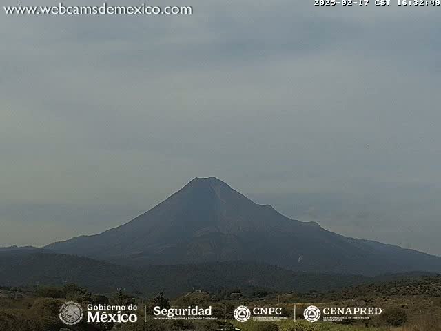 A large, dark-colored volcano is visible under a mostly cloudy, light gray sky.