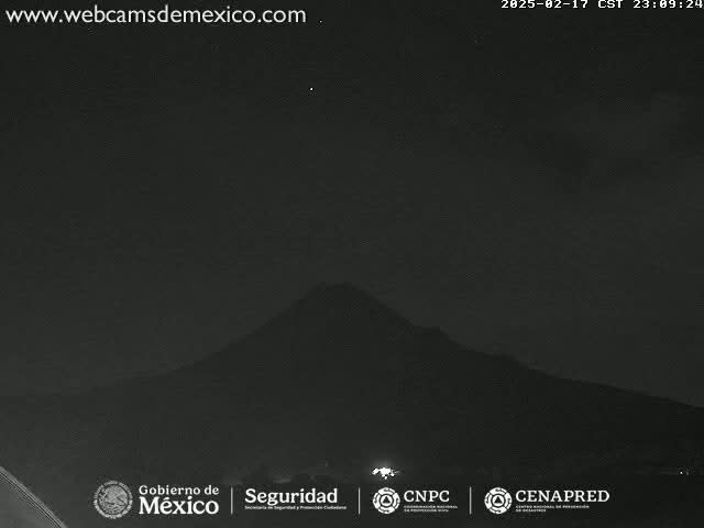 A nighttime, low-light view shows a dark mountain silhouetted against a mostly clear sky.