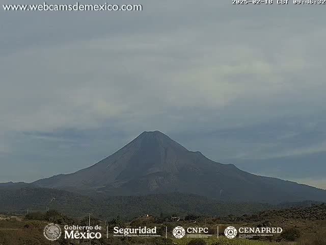 A large, dark-colored volcano is visible under a mostly cloudy, overcast sky.