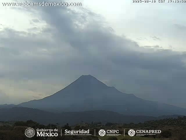 A large, dark-colored volcano is visible in the distance under a mostly cloudy sky.