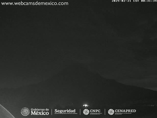 A dark, nighttime view of a mountain range under a mostly clear sky.