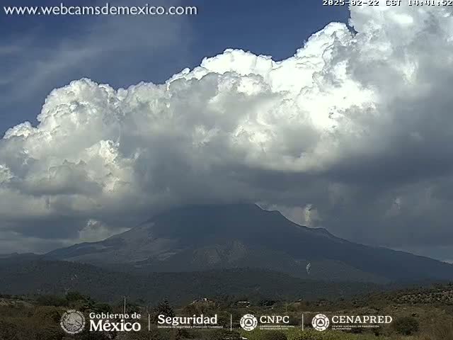A large, dark cumulus cloud formation looms over a dark, mountainous landscape under a partly cloudy sky.