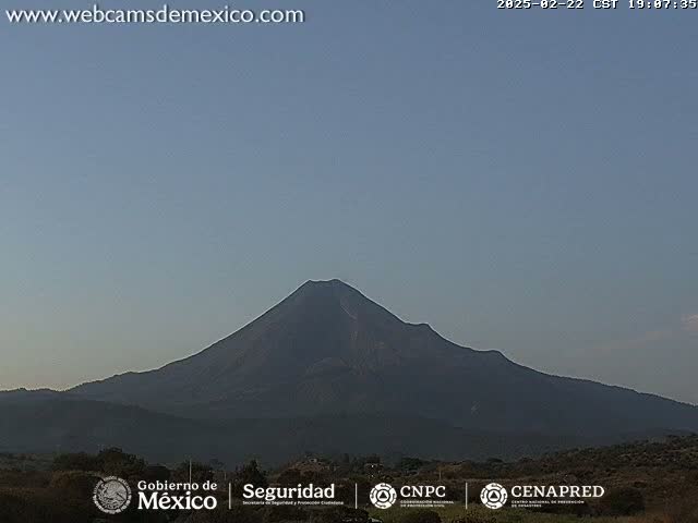 A large, dark-colored volcano is visible against a clear, light-blue sky.