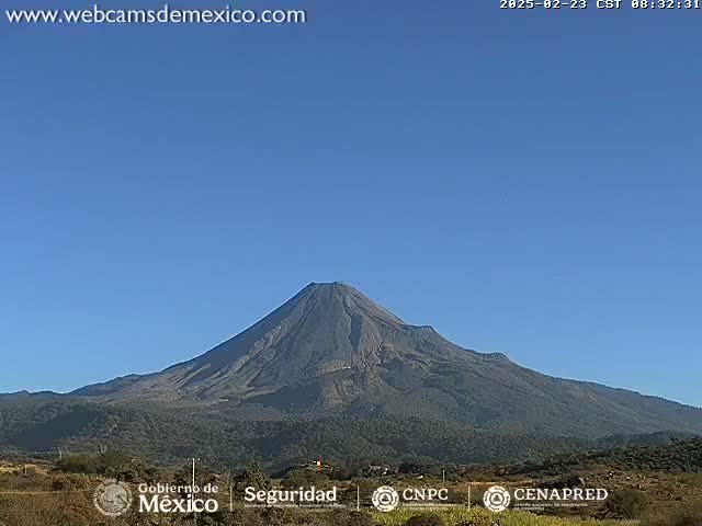 A large, dark-colored volcano is seen under a clear blue sky.