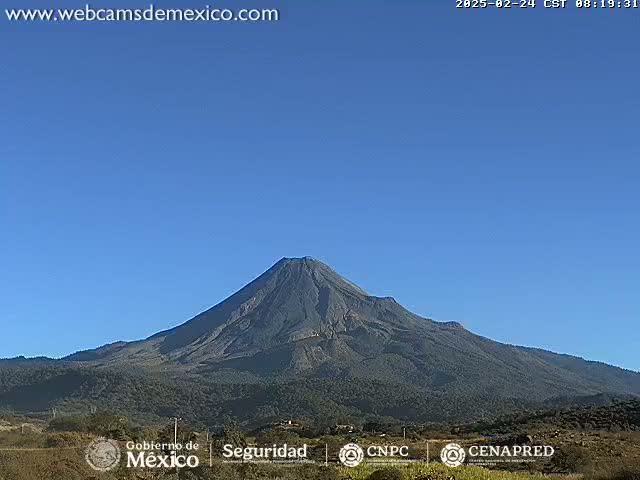 A large, dark-colored volcano is seen under a clear, blue sky.