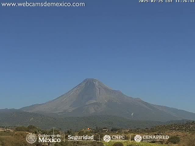 A large, dark-gray volcano is visible under a clear blue sky.