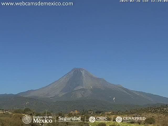 A large, dark-colored volcano is visible under a clear blue sky.