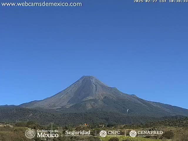 A large, dark-colored volcano is visible under a clear blue sky.