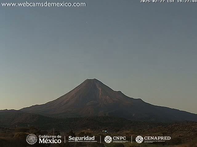 A large, dark-colored volcano is visible under a clear, light-blue sky.