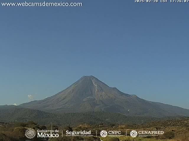 A large, dark-colored volcano is visible under a clear, light-blue sky.