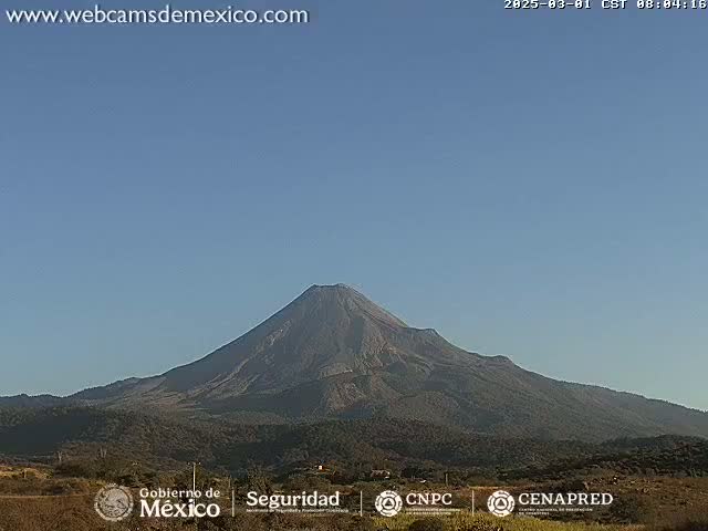 A large, dark-colored volcano is seen under a clear blue sky.