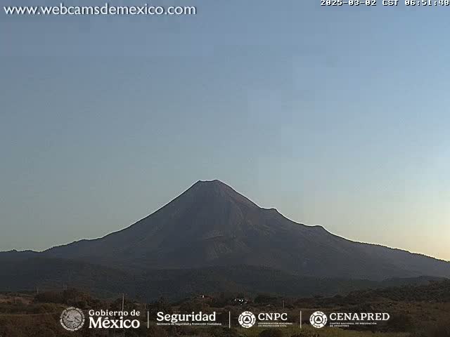 A large, dark-colored volcano is visible against a clear, light-blue sky.