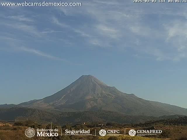 A large, dark-colored volcano is visible under a mostly clear, light-blue sky with a few scattered clouds.