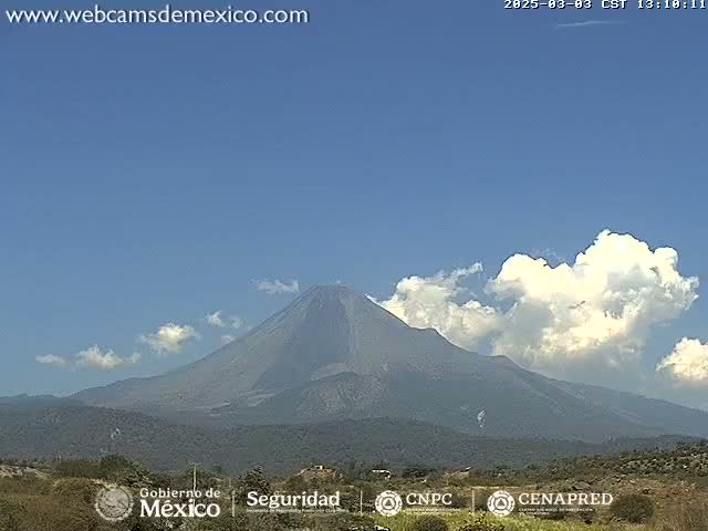 A large volcano is visible under a mostly clear sky with some fluffy white clouds.