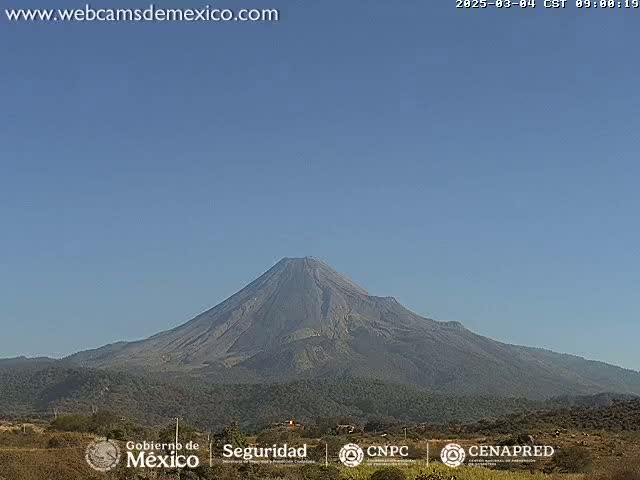 A large, dark-grey volcano is visible against a clear, light-blue sky.