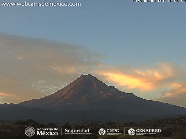 A large, dark volcano is silhouetted against a twilight sky with streaks of orange and yellow clouds.