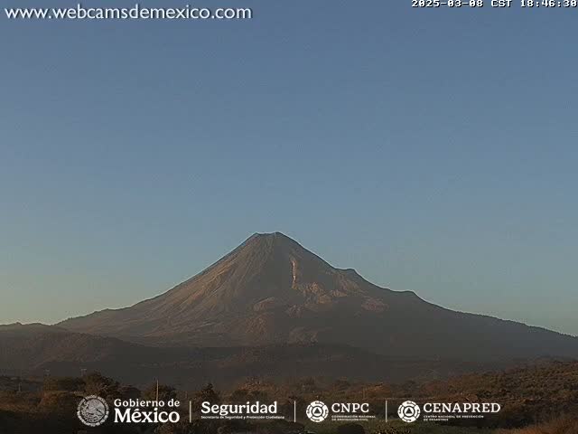 A large, dark-colored volcano is visible against a clear, pale blue sky.