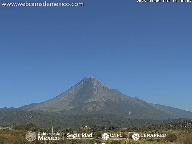 A large, dark gray volcano is visible under a clear blue sky.