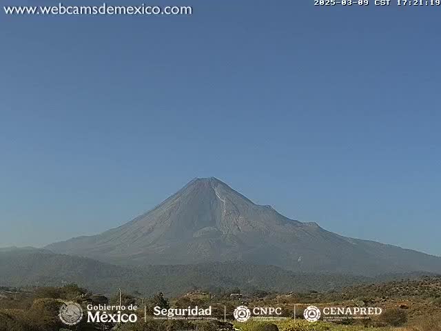 A large, dark-grey volcano is visible under a clear blue sky.