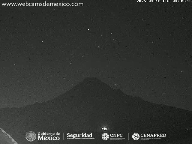 A nighttime long shot of a dark mountain silhouetted against a clear, starry sky.