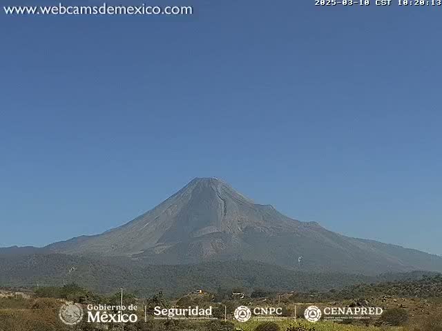 A large, dark-grey volcano is visible under a clear, blue sky.