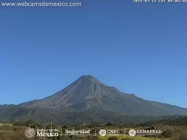 A large, dark-colored volcano is visible under a clear blue sky.
