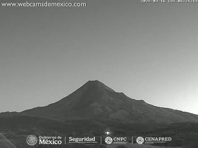 A large, dark-colored volcano is visible under a clear, light gray sky.