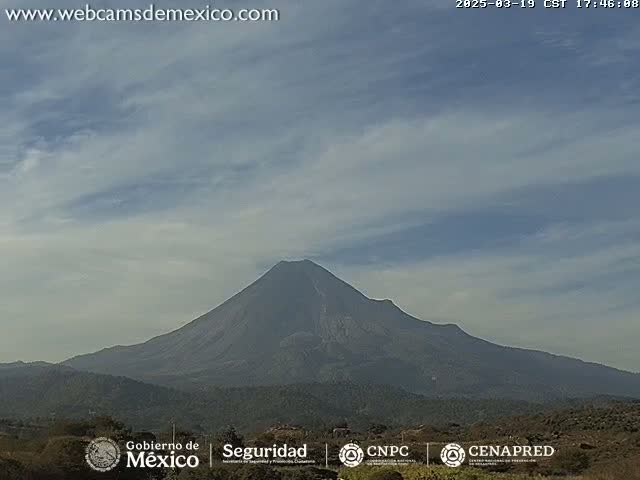 A large, dark-colored volcano is visible under a mostly cloudy sky.