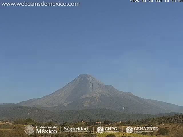 A large, dark-grey volcano is visible against a clear, light-blue sky.
