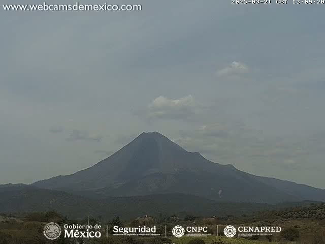 A large, dark volcano is visible in the distance under a mostly cloudy sky.