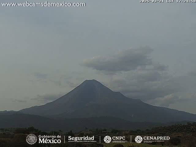 A large, dark-colored volcano is visible under a mostly cloudy, overcast sky.