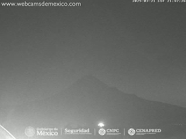 A nighttime, low-light image shows a dark, hilly landscape under a mostly clear sky.