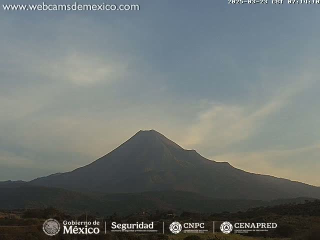 A large, dark volcano is visible under a mostly clear, light-blue sky.