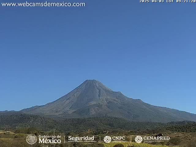 A large, dark-colored volcano is seen under a clear blue sky.
