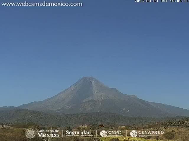 A large, dark-grey volcano is visible under a clear, blue sky.