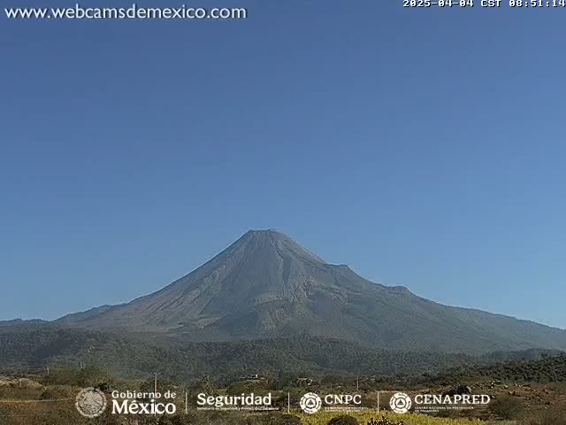 A large, dark-colored volcano is seen on a clear, sunny day.