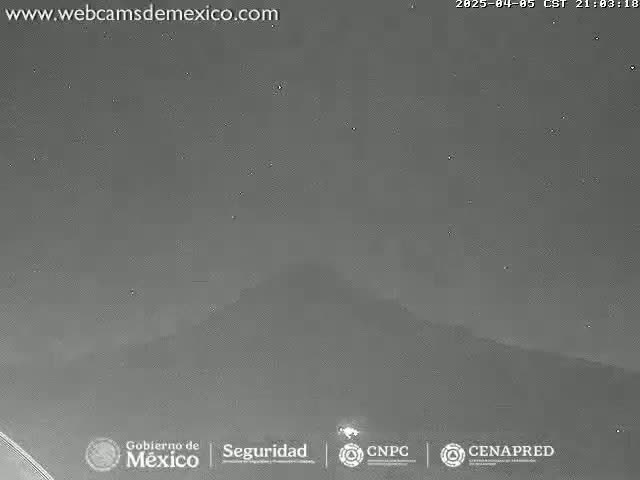 A nighttime, low-light image shows a dark, mostly clear sky over a hilly or mountainous landscape.