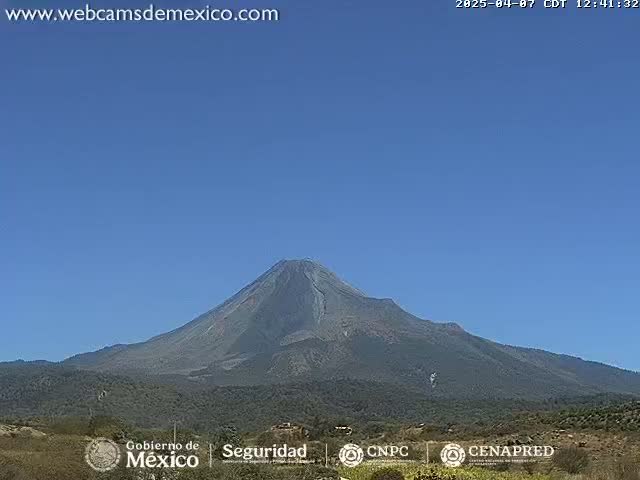 A large, dark-gray volcano is visible against a clear, bright blue sky.