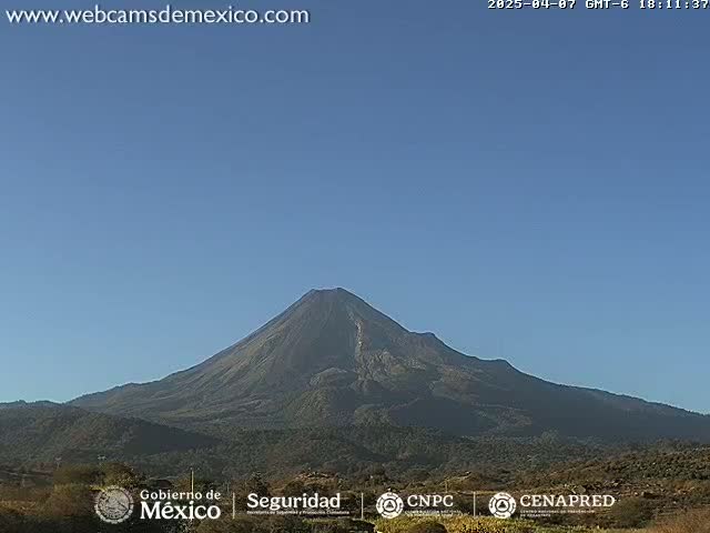 A large, dark-colored volcano is seen on a clear, sunny day.