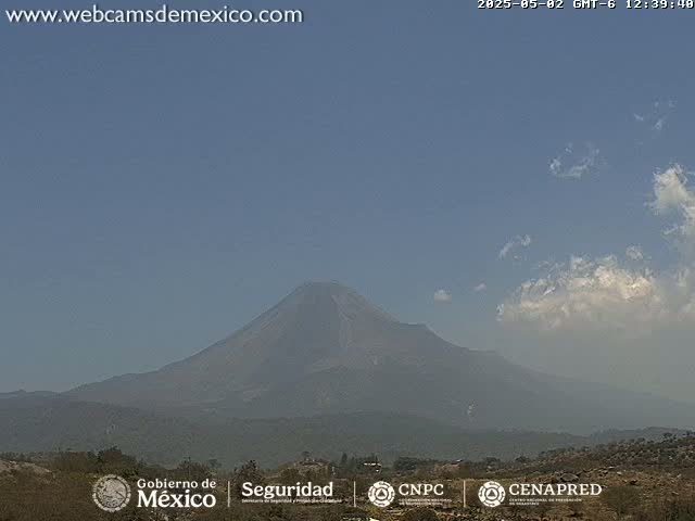 A hazy, partly cloudy day reveals a large, dark volcano in the distance.