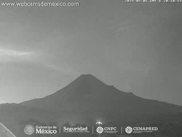 A grayscale image shows a large, dark mountain under a mostly clear, light gray sky.