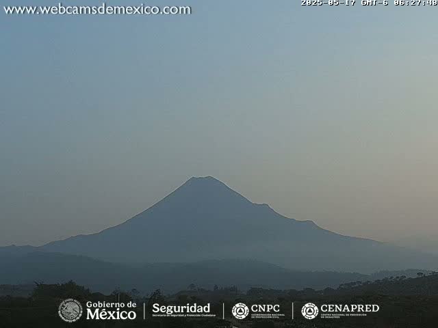 A hazy, distant view of a large, dark mountain range under a pale sky.