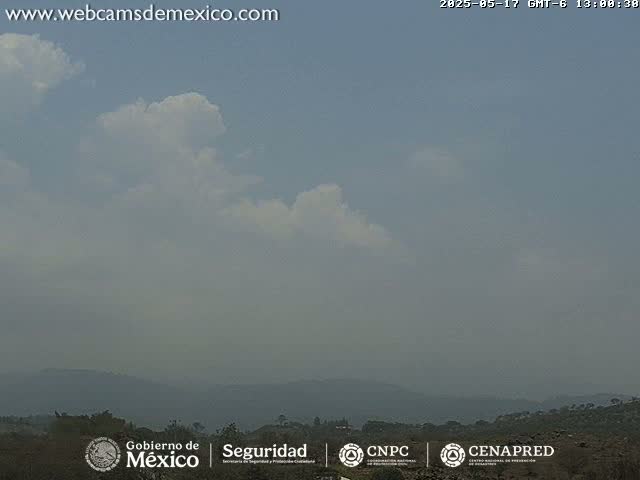 A hazy sky with a few cumulus clouds partially obscures distant, low-lying mountains.
