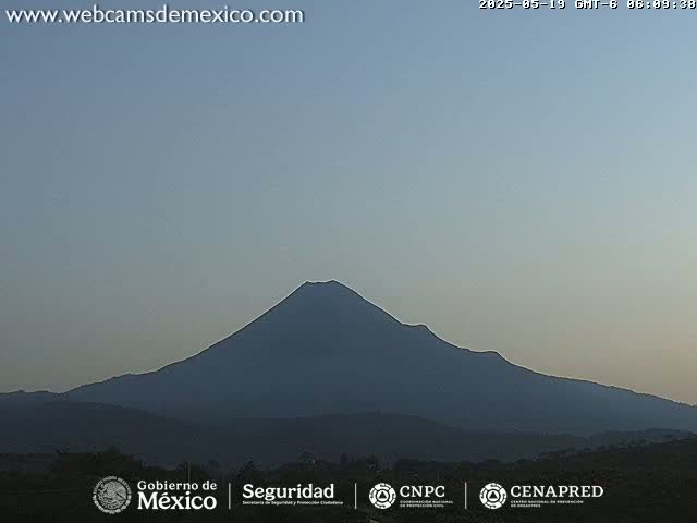 A large, dark-colored volcano is seen under a clear, dusky sky.