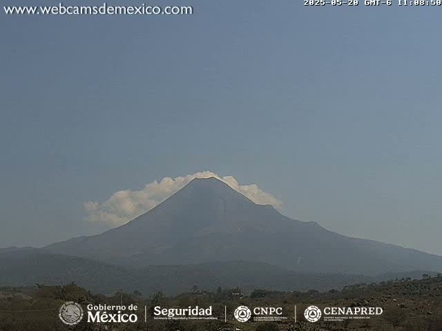 A large, dark volcano with a small amount of cloud cover is visible under a clear, light-blue sky.