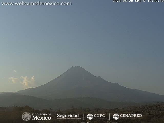 A large, dark volcano is visible against a pale, clear sky with a few wispy clouds.