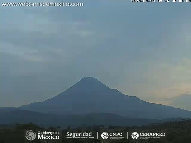 A large, dark-colored volcano is visible against a hazy, light-blue sky.