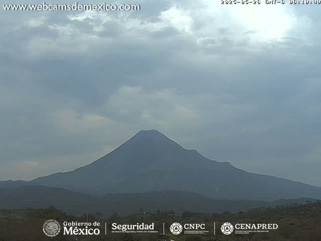 A large, dark-colored volcano is visible under a mostly cloudy sky.