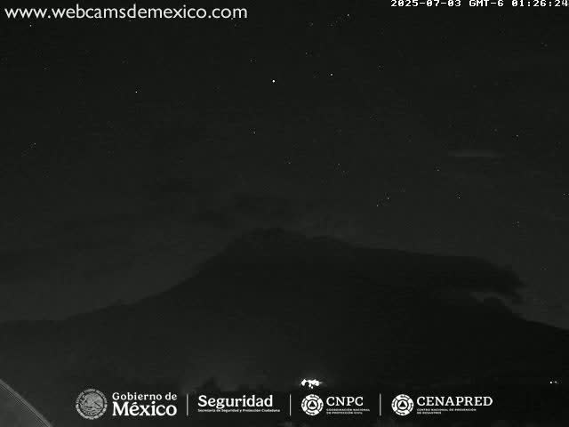 A nighttime, low-light view shows a dark mountain silhouetted against a mostly clear sky dotted with stars.